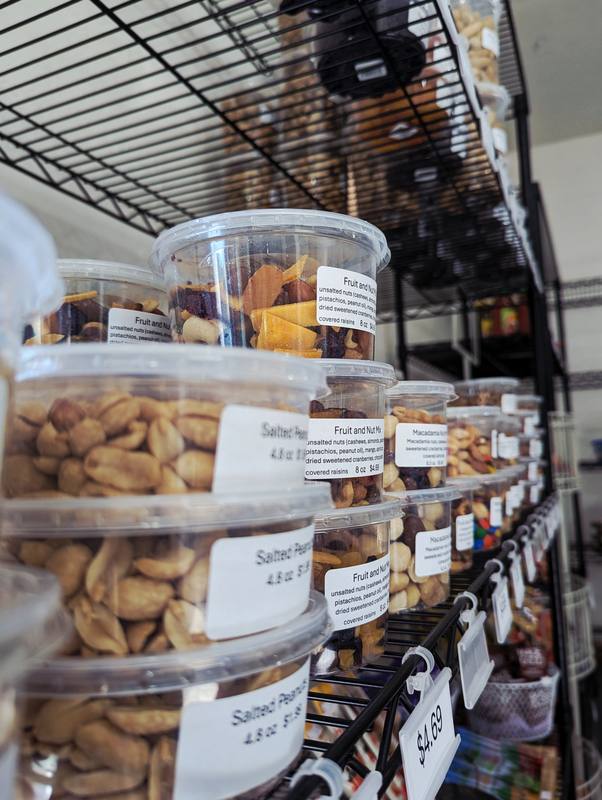 Stacked clear tubs of salted peanuts, fruit and nut mix and macadamia mix on a wire shelf.