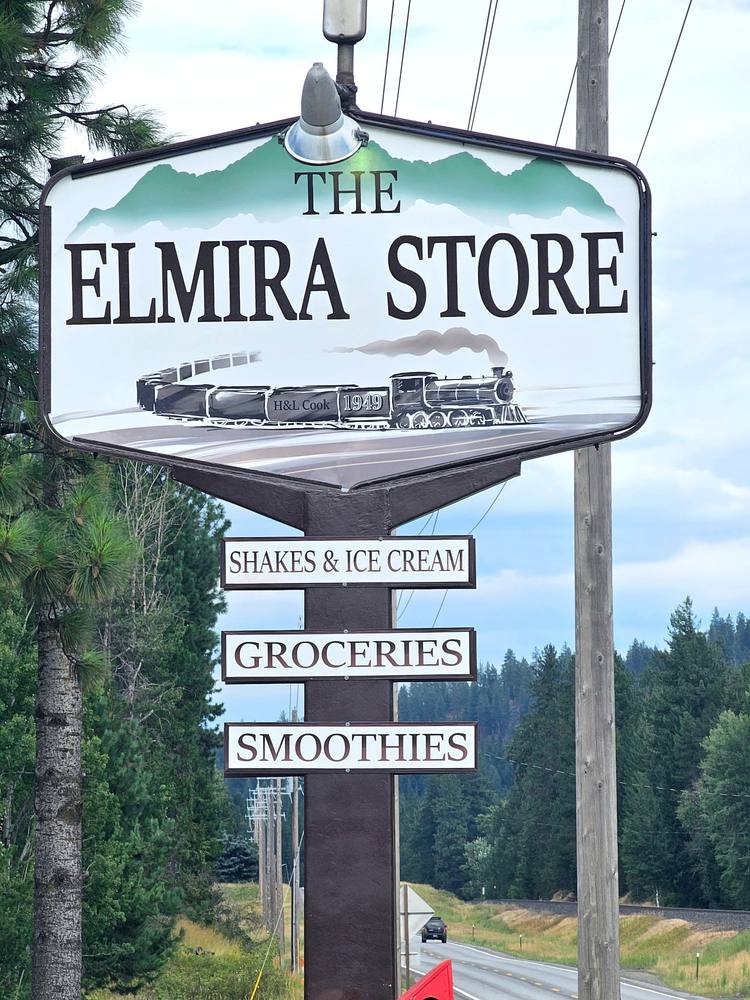 The Elmira Store's roadside sign on Highway 95, painted with a steam locomotive and the year 1949, with panels reading Shakes & Ice Cream, Groceries, and Smoothies.