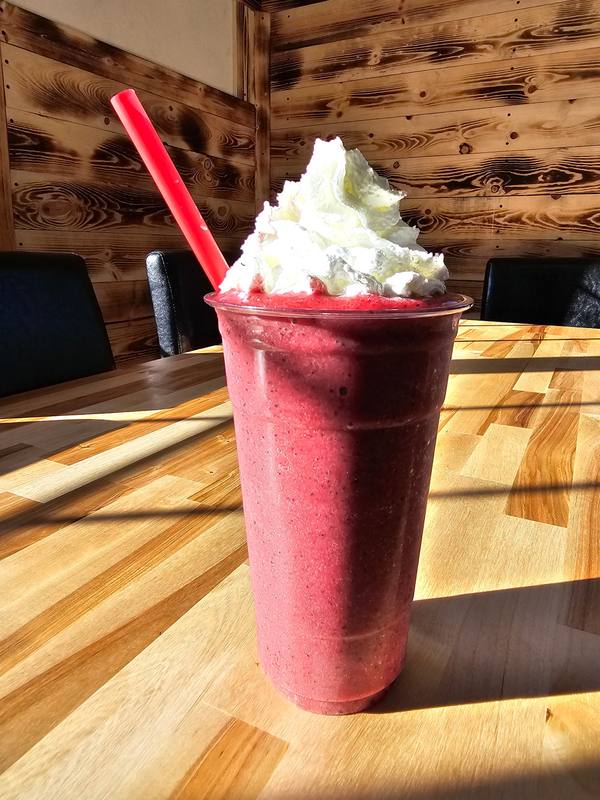 A tall berry smoothie topped with whipped cream on a butcher-block table in the window light.